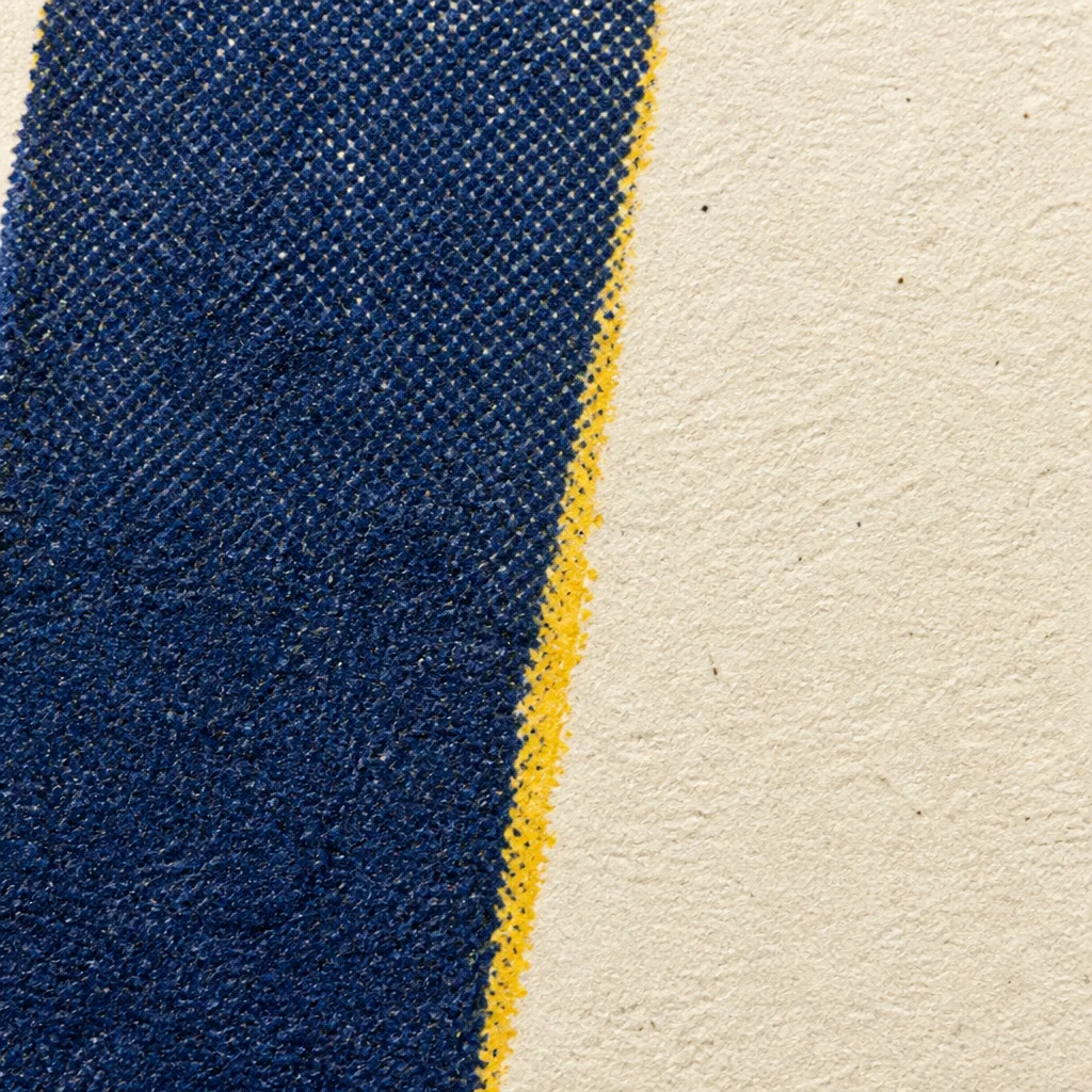 Macro screenprint detail: the edge of a thick indigo ink stroke on cream paper, with a chrome yellow underprint showing along one side where the press ran out of register.