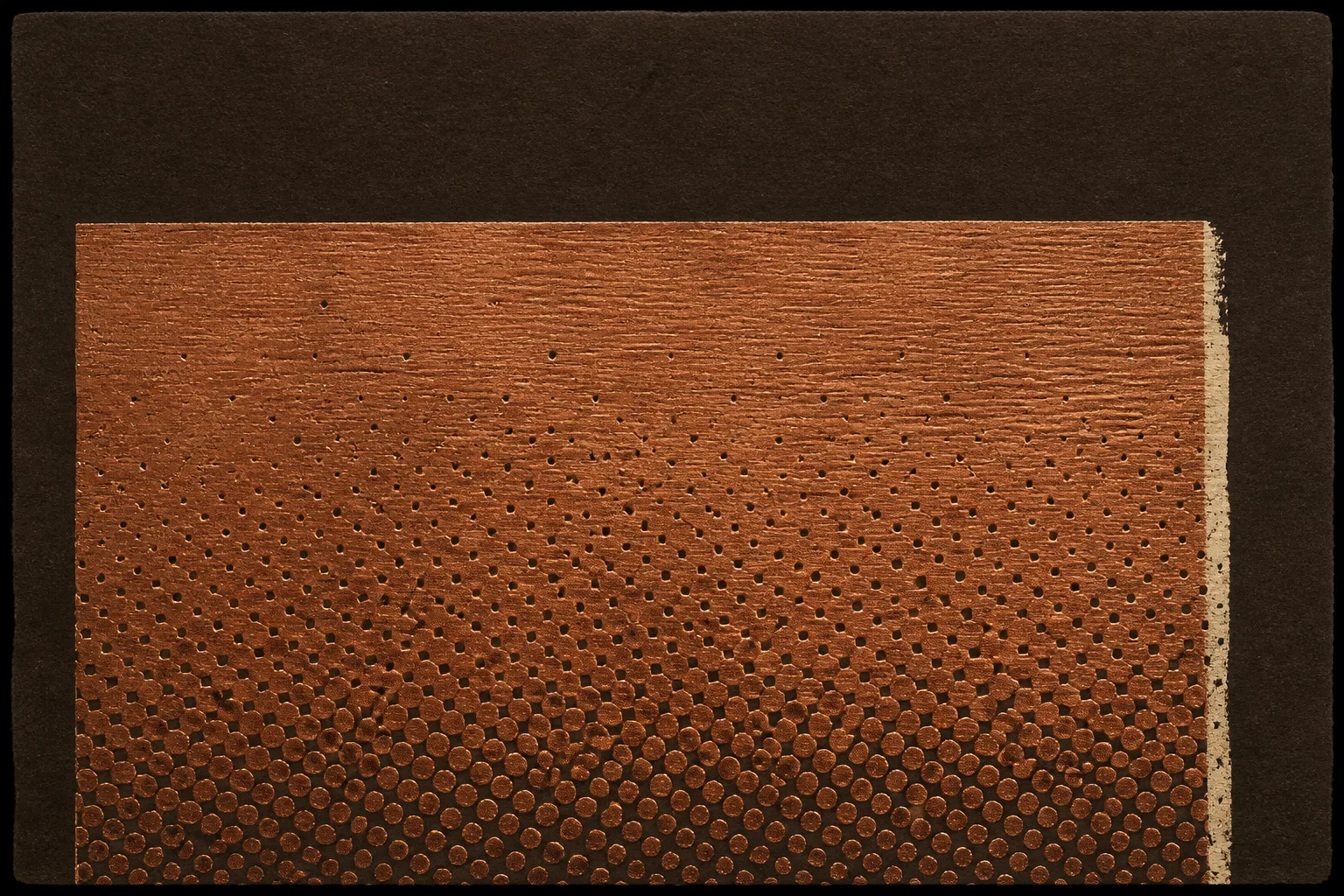 Close woodblock proof in copper ink on dark umber paper: a single flat rectangle showing carved wood grain and a coarse halftone dot field, dense at the bottom and fading toward the top, with a thin cream misregistered edge along the right side