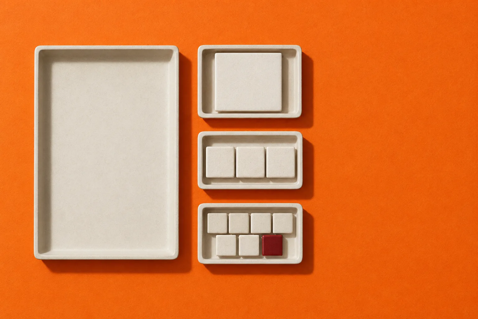 Overhead photograph on tangerine paper: a large empty ceramic tray, and beside it three small trays holding one tile, three tiles in a row, and seven tiles wrapped four over three, the last of them oxblood red.