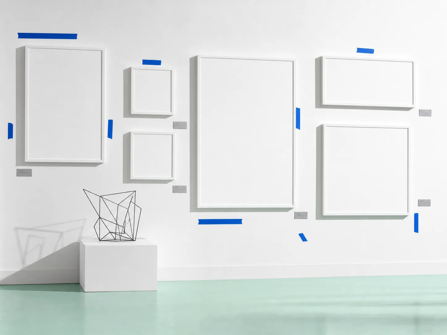 White gallery wall with blank frames, cobalt tape, and an abstract wire sculpture.